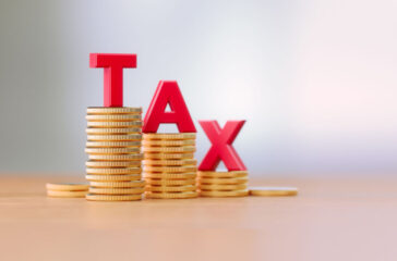 Tax Reduction Concept - Red Letters Sitting On Coin Stacks Write Tax Before Defocused Background