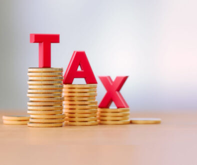 Tax Reduction Concept - Red Letters Sitting On Coin Stacks Write Tax Before Defocused Background